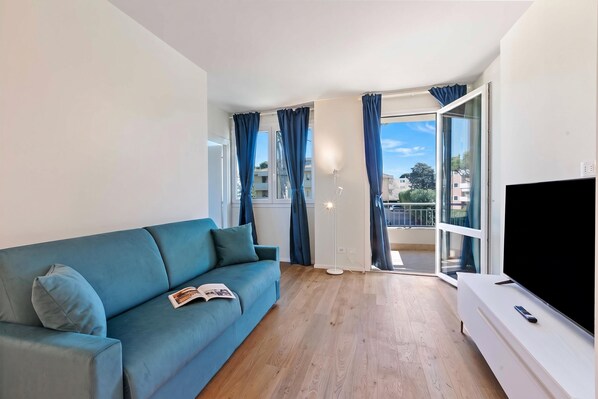A living room with a sofa, a flat-screen TV, and a balcony with curtains. - Tintoretto Apartments (Camaiore)