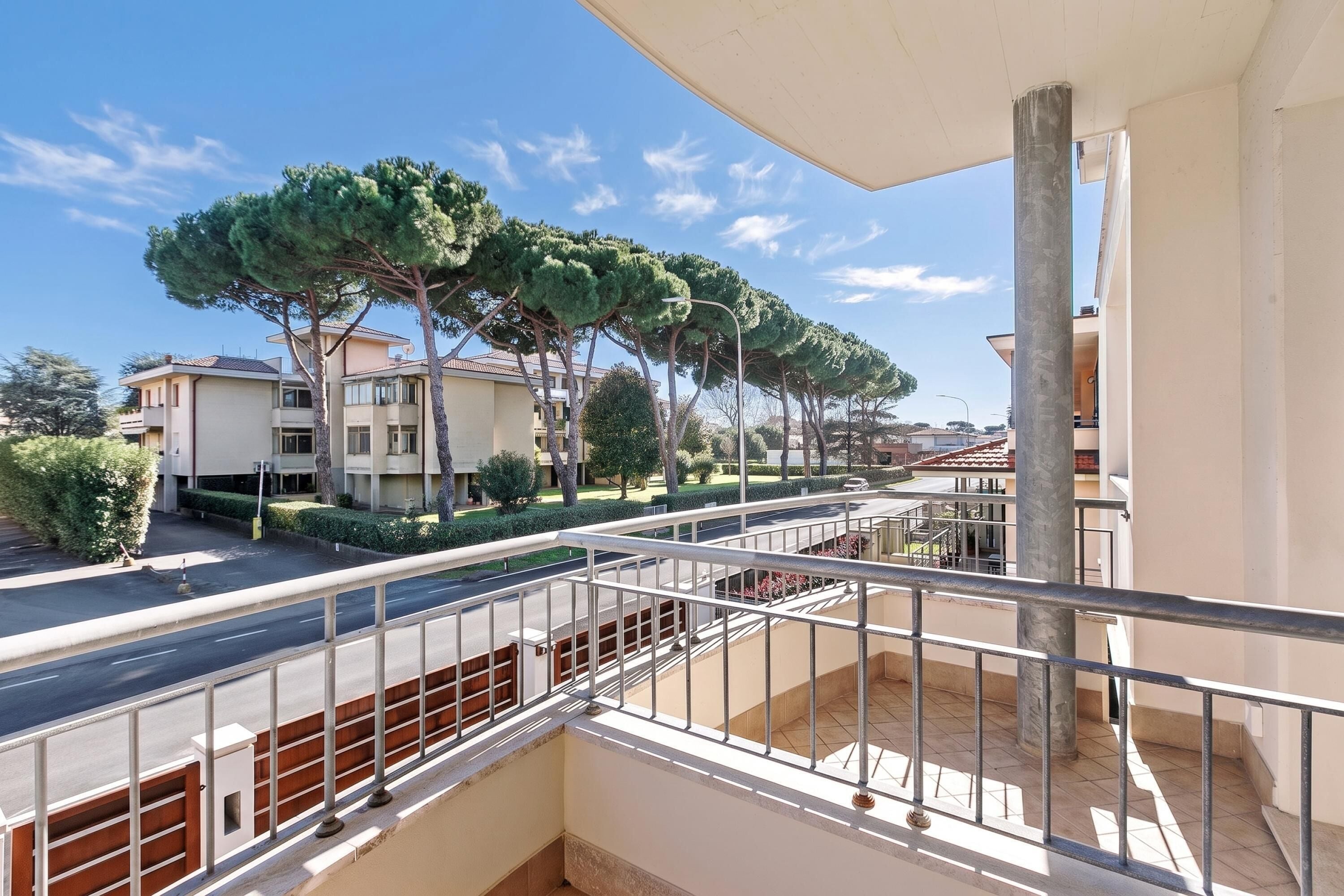 A residential building with a balcony, a street view, and trees.
