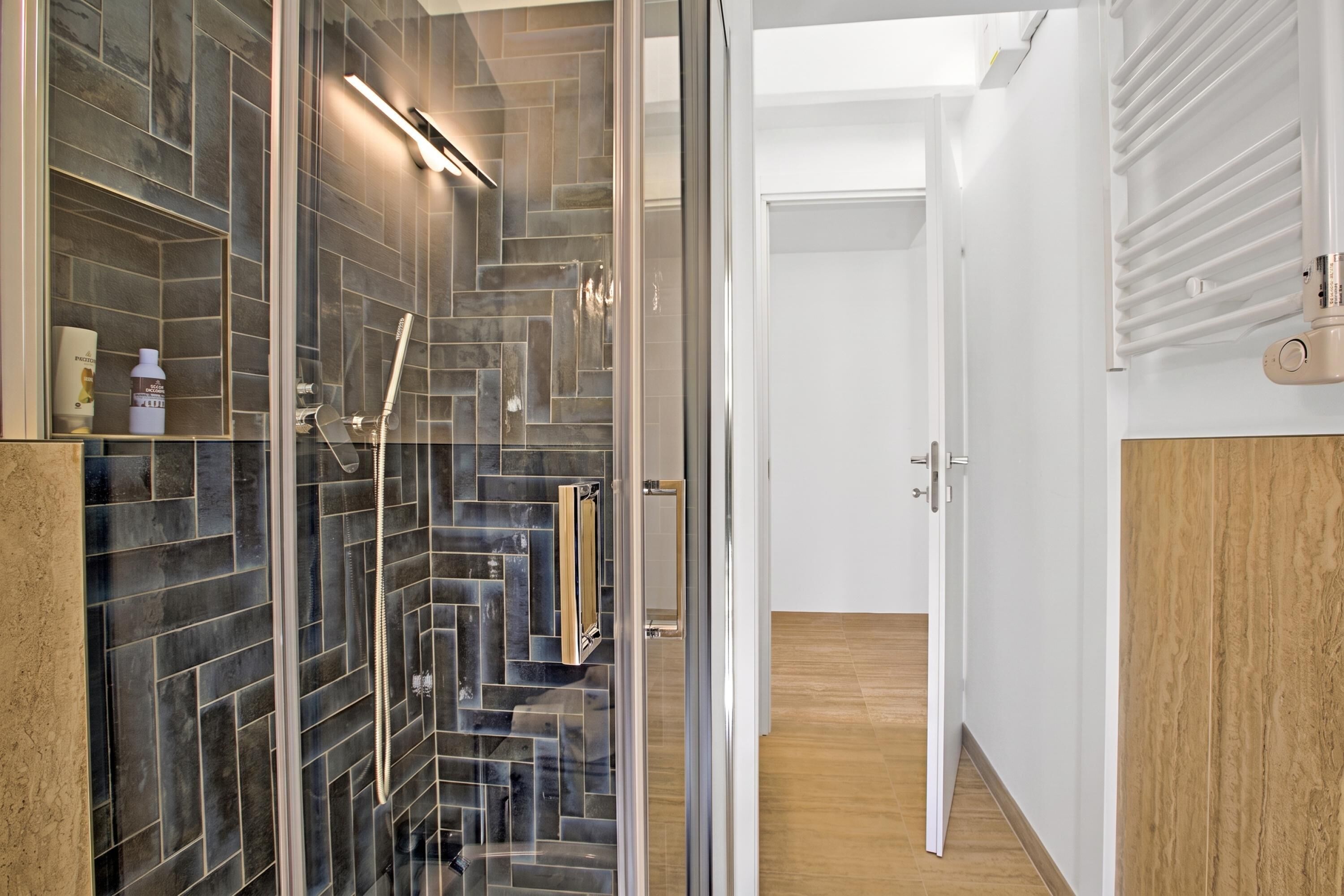 Een moderne badkamer met een douchecabine van glas, een houten vloer en een witte deur die naar een andere kamer leidt.