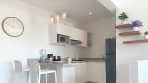 A modern kitchen with white cabinetry, a built-in microwave, a black refrigerator, and a marble floor. There are two white bar stools and a clock on the wall.