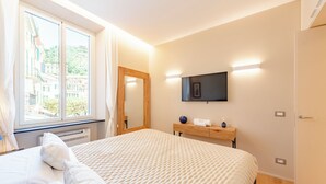 A hotel room with a large bed, a wooden nightstand, a flat-screen TV mounted on the wall, and a window with curtains. - A dreamlike apt in Piazzetta Portofino (Portofino)