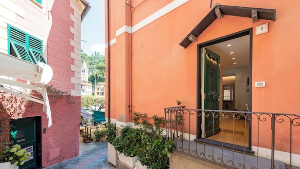 A building with a red and white facade, a balcony with metal railings, and potted plants. - A dreamlike apt in Piazzetta Portofino (Portofino)