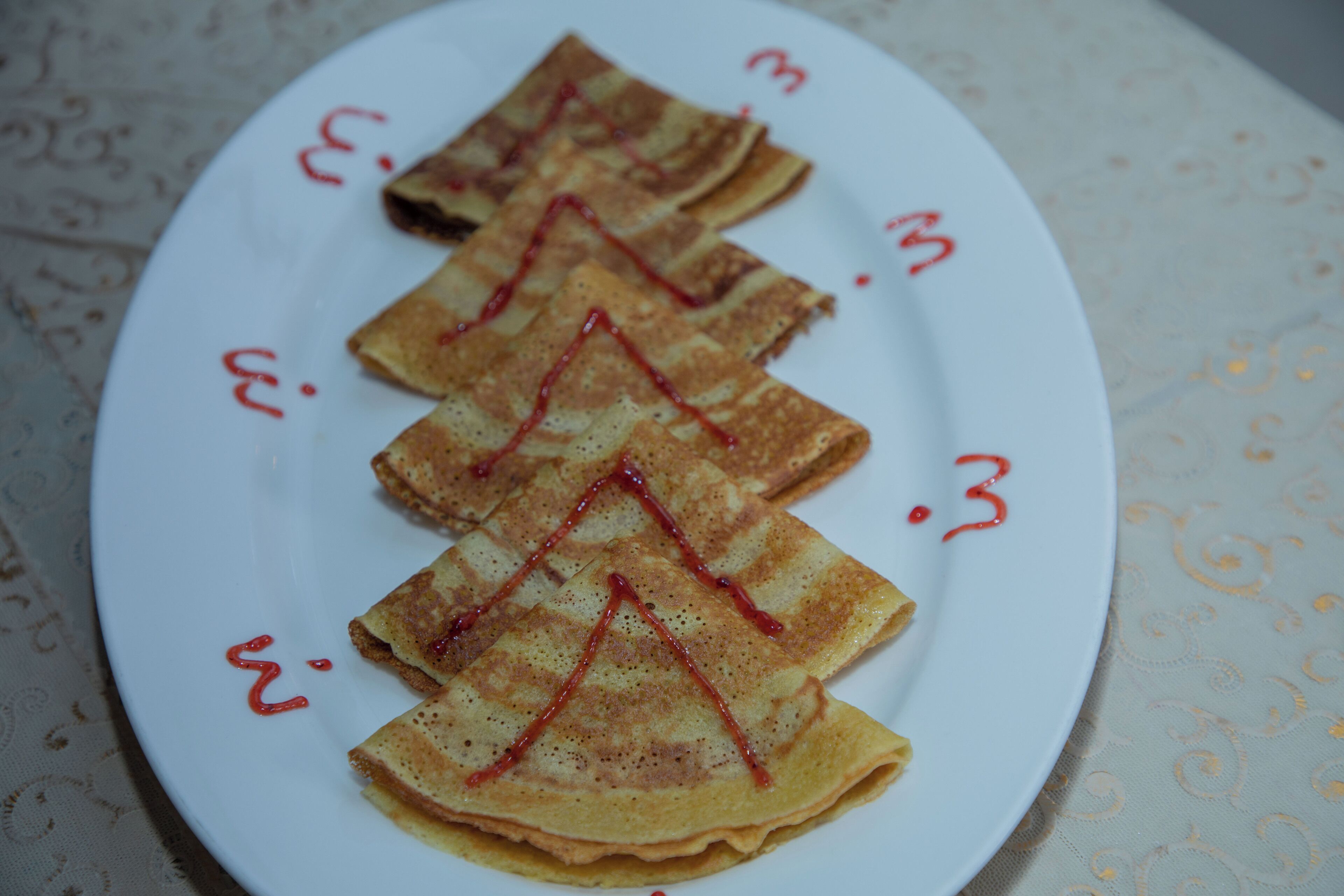 A plate of crepes with red sauce on a tablecloth.