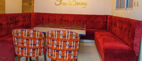 Comedor con un banco tapizado en rojo, una mesa con cubierta de vidrio y sillas estampadas.