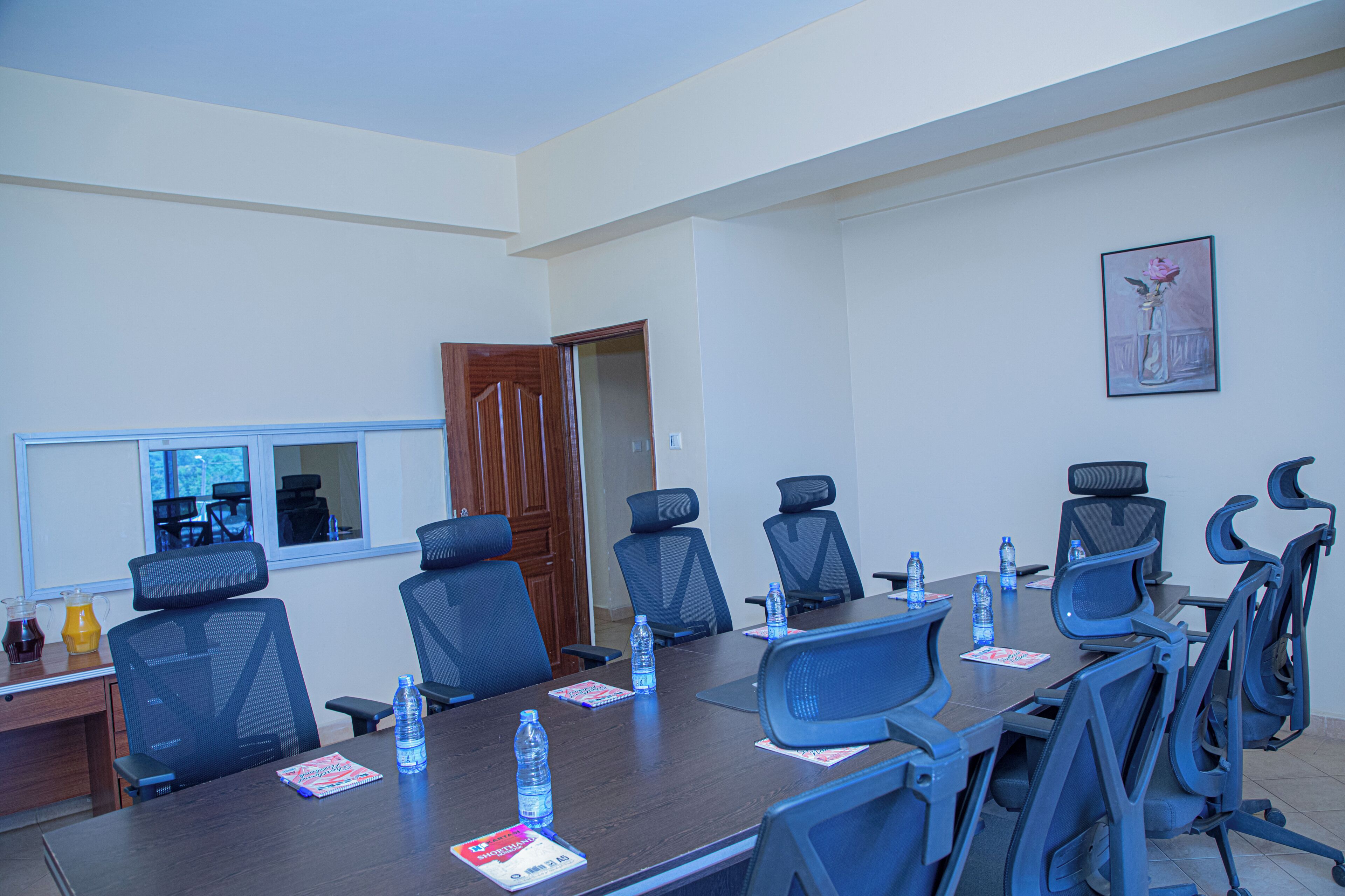 Una sala de conferències amb una taula llarga, cadires, ampolles d'aigua i una porta que condueix a una altra sala.