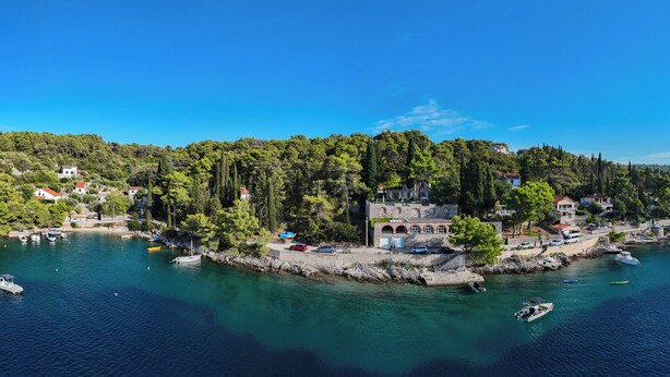 A coastal village with a stone building surrounded by trees, boats docked along the shore, and a clear blue sky. - Dream property right on the water (Rogač)