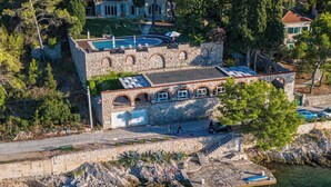 An aerial view of a coastal property with a stone building, a swimming pool, and a dock extending into the sea. - Dream property right on the water (Rogač)