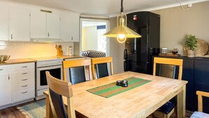 Una cocina compacta con armarios blancos, un refrigerador negro y una mesa de comedor de madera con sillas.