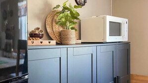 Una cocina con un microondas sobre un mueble, una cesta tejida y una planta en maceta.