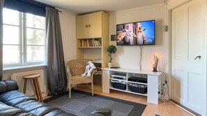 Un salón con sofá, sillón, estantería, televisor y puerta.