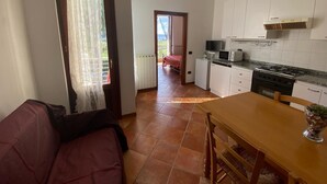 A compact kitchen with white cabinets, a stove, a microwave, and a dining area with a wooden table and chairs.