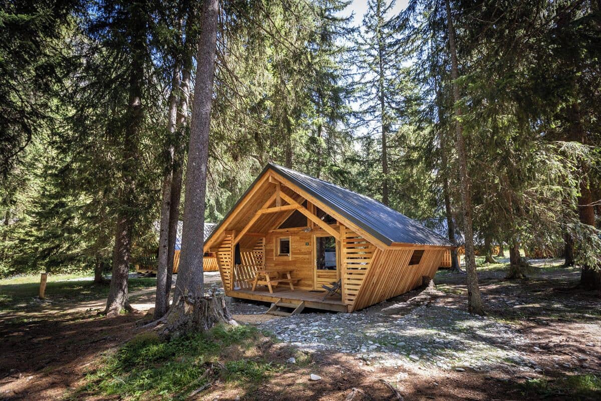 Eine Holzhütte mit geneigtem Dach, umgeben von hohen Bäumen.