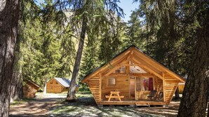 A wooden cabin with a porch, a picnic table, and a clear view of the surrounding forest.