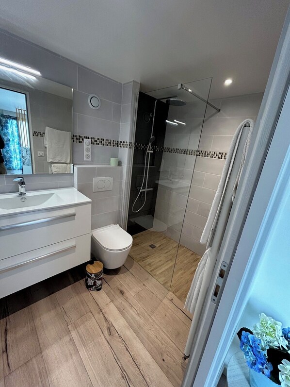 A modern bathroom with a white vanity, a toilet, a glass-enclosed shower, and a wooden floor.