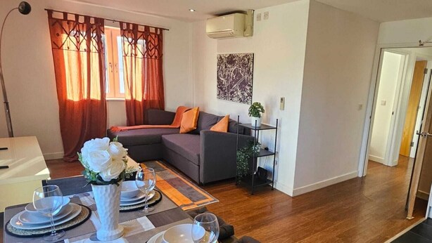 Ein modernes Wohnzimmer mit einer Couch, einem Esstisch für vier Personen und einer Küchenzeile im Hintergrund.