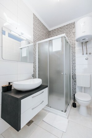 Une salle de bain moderne avec un lavabo blanc, une douche en verre et des toilettes.
