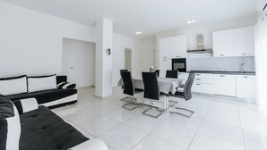 A modern living room with a black and white sofa, a dining table with chairs, and a kitchen area with white cabinets and a stove. - Apartments Lola (Novalja)