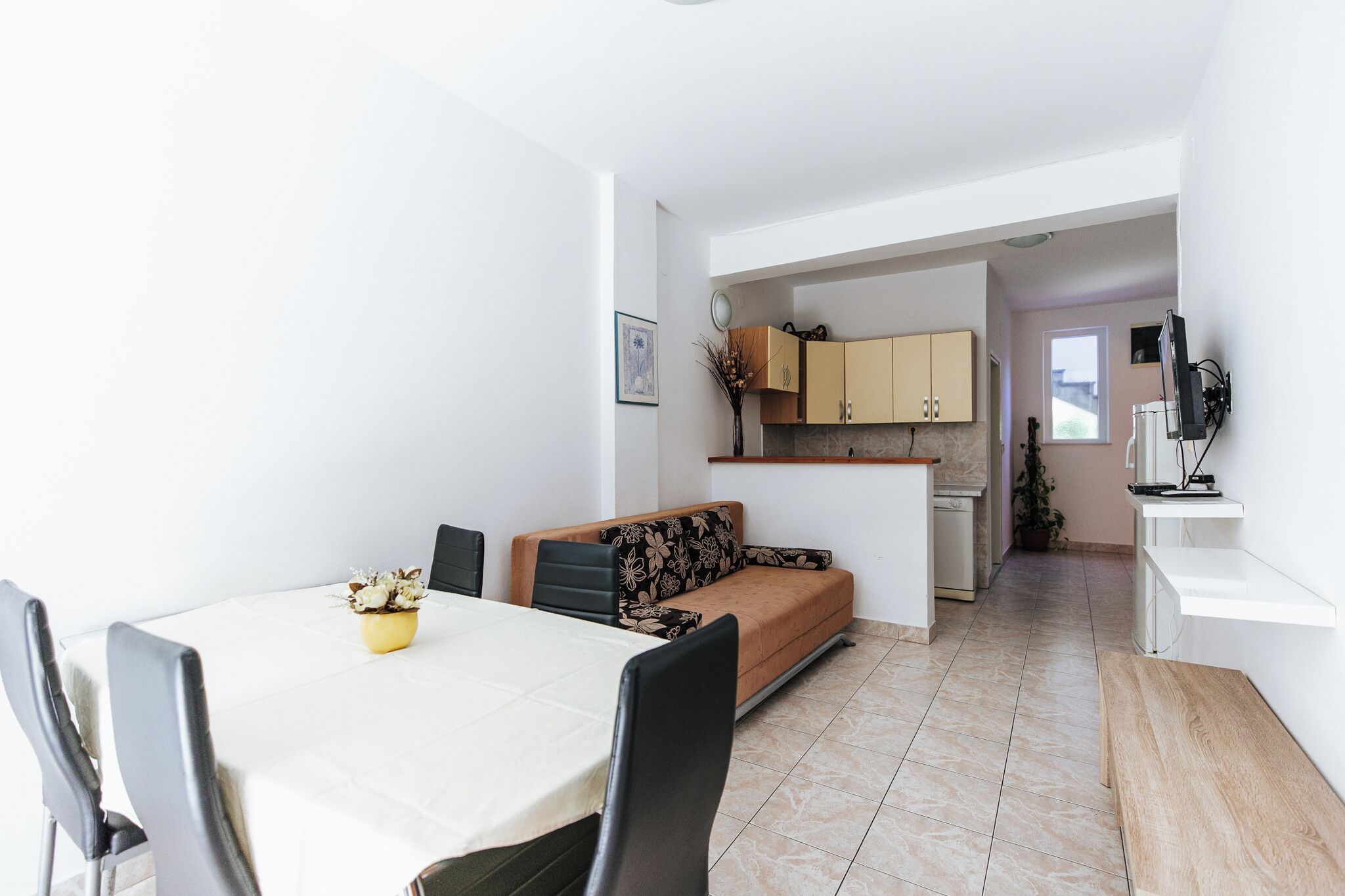 A dining area with a table, chairs, and a sofa. There is a kitchen in the background with cabinets and a sink.