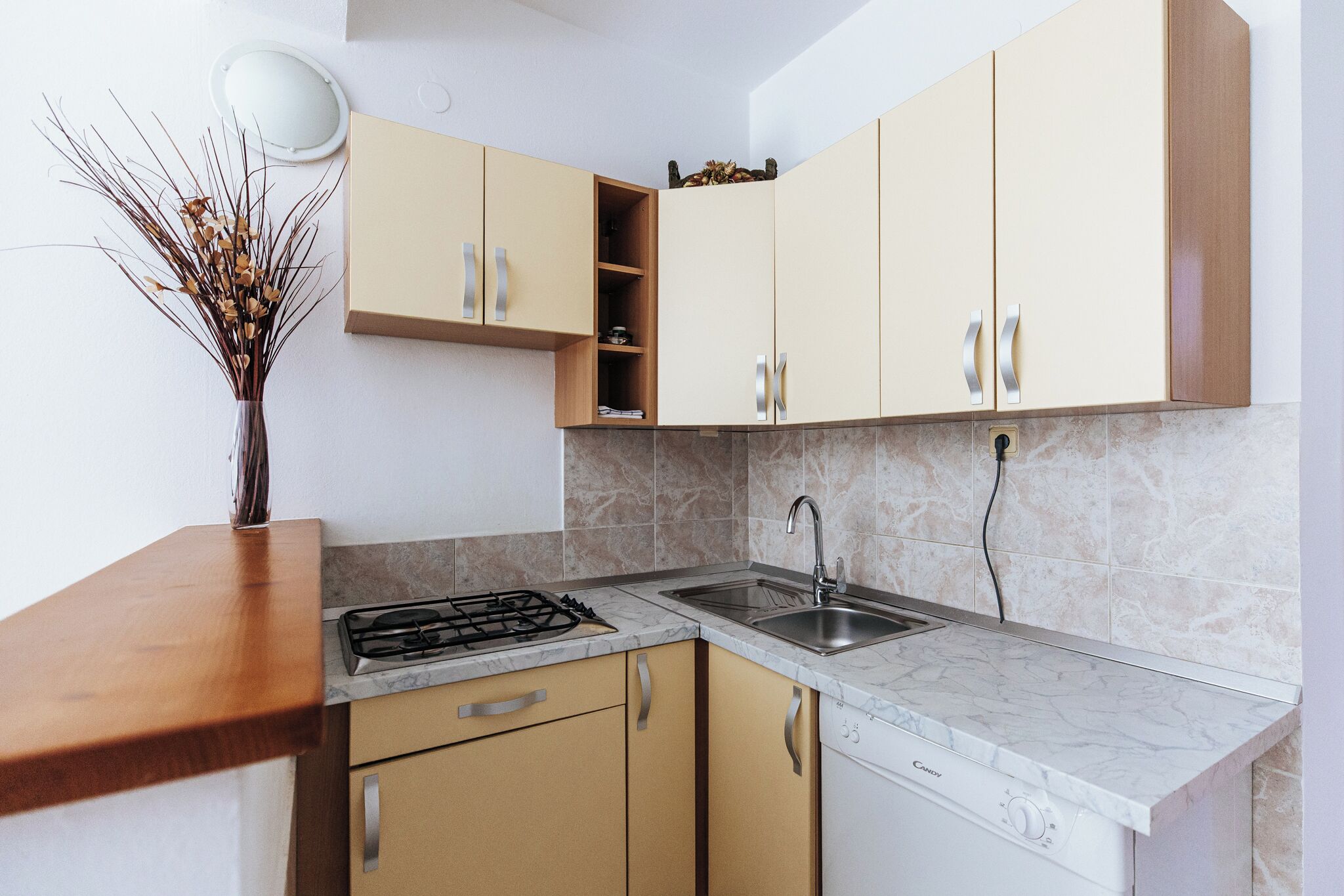 Une cuisine moderne avec des meubles de couleur beige, un plan de travail en marbre, une cuisinière à gaz, un évier et un lave-vaisselle.