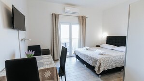 A hotel room with a bed, a TV mounted on the wall, a table with a chair, and a window with curtains. - Apartments Lola (Novalja)