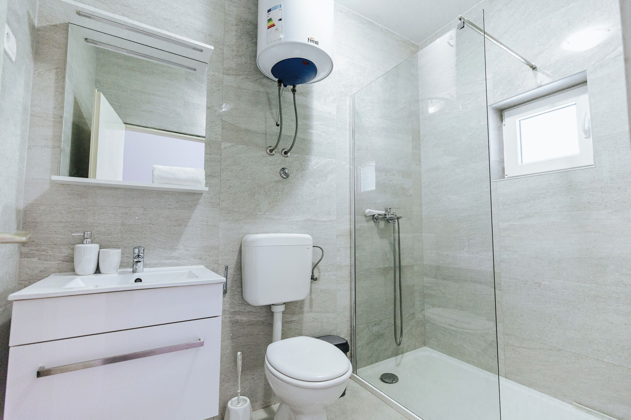 A modern bathroom with a glass-enclosed shower, a white sink with a mirror above it, and a toilet.