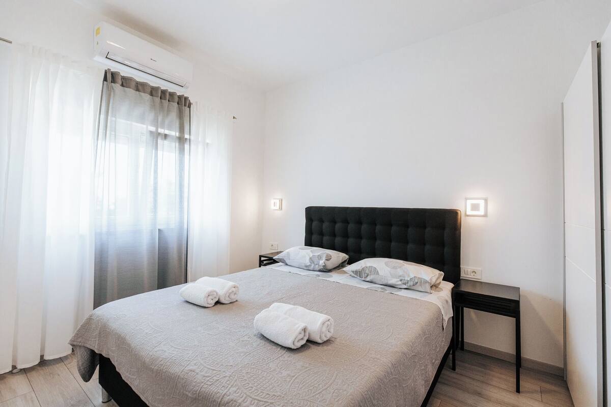 A neatly made bed with two rolled towels, a dark headboard, and bedside lamps.