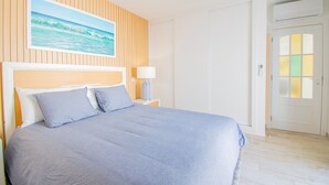 Ein Schlafzimmer mit Bett, Nachttisch, Lampe, Gemälde und einer Tür mit satiniertem Glas.