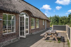 A brick building with a thatched roof, large windows, and a wooden table outside.