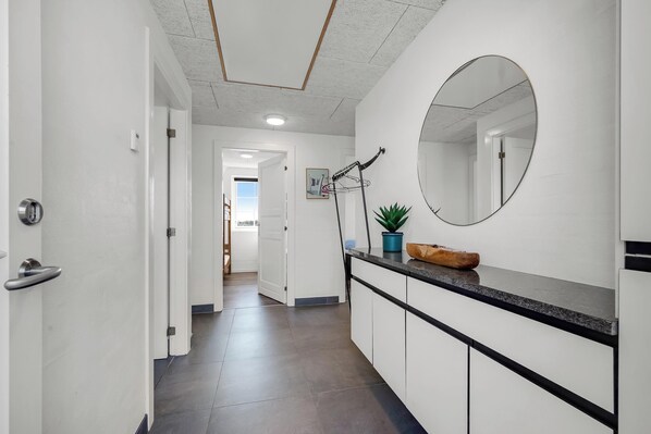 A hallway with a white door, a mirror, a potted plant, and a counter with a towel.