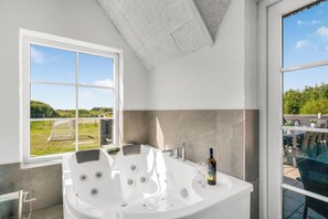 A modern bathroom with a large bathtub, a glass shower enclosure, and a view of a garden through a large window. - Large 16-person holiday home with pool, hot tub and sauna (Ulfborg)