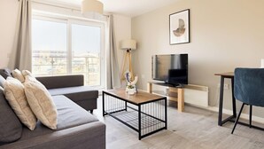 A modern living room with a sofa, coffee table, TV, and a view of the city. - 2 Bedrooms Apartment in Wembley (Wembley)
