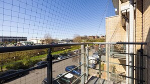 A view from a window with a metal grid, overlooking a parking lot with several cars and a building in the background. - 2 Bedrooms Apartment in Wembley (Wembley)