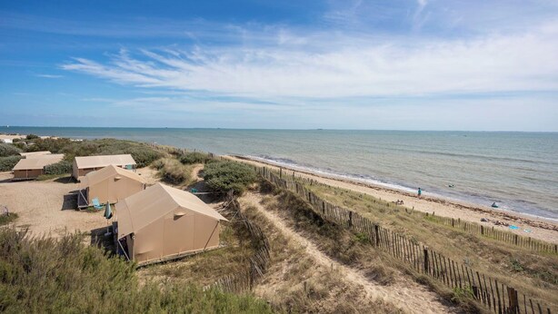 Een verblijfsgebied aan het strand met tenten en een zandpad naar de zee.