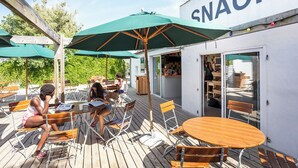 Een terras met houten tafels en stoelen, groene parasols en een gebouw met de tekst 