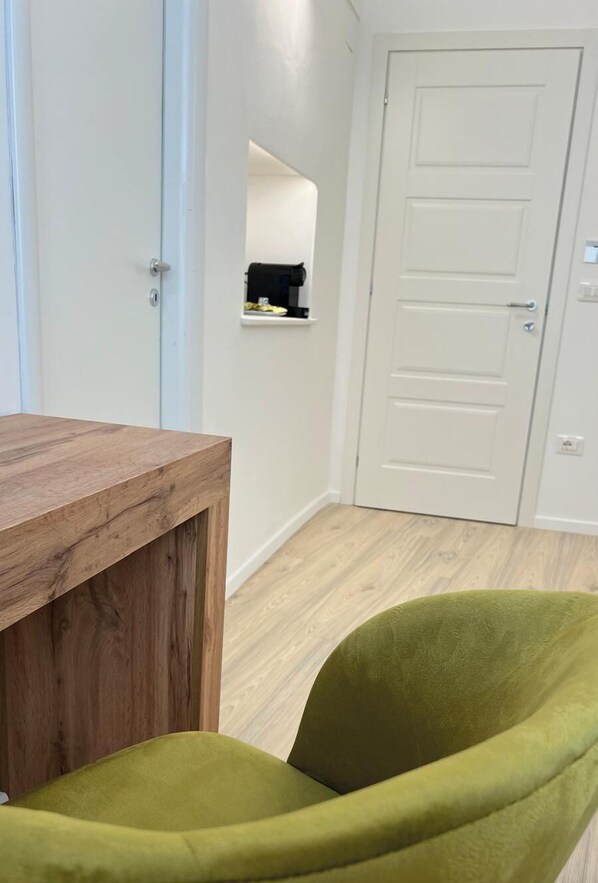 A room with a wooden desk, a green chair, a white door, and a small shelf with items on it. - Suite Duomo Tropea (Tropea)