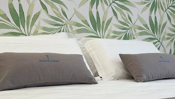 Una cama con dos almohadas, cabecera blanca y pared con diseño de hojas.