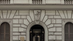 Fachada de edificio con un arco central, flanqueado por dos ventanas con contraventanas y un relieve de piedra decorativo sobre el acceso.