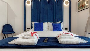 Habitación de hotel con una cama grande, cabecera azul, ropa de cama blanca y un control remoto sobre la cama.