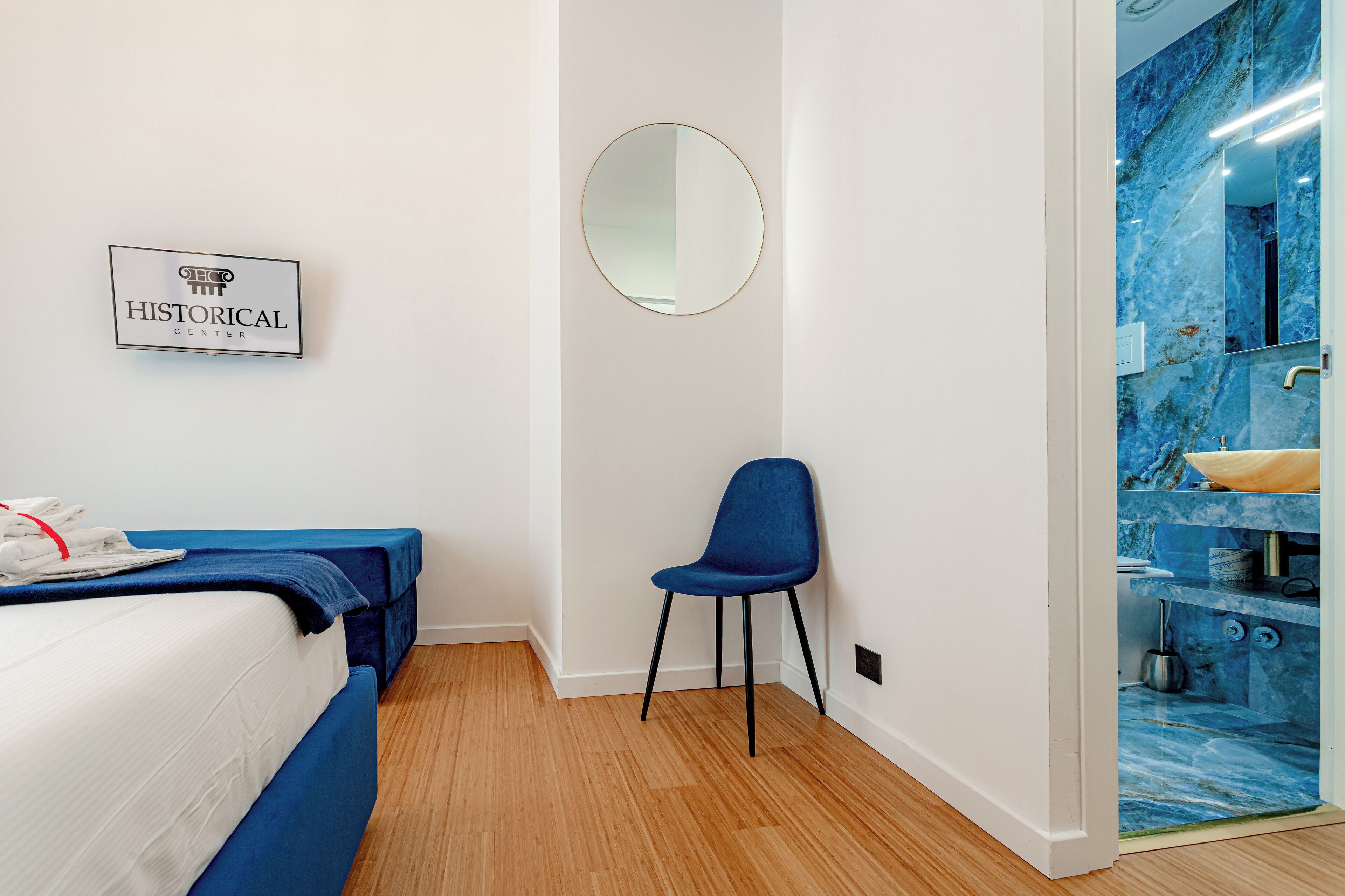 A hotel room with a bed, a chair, a mirror, and a bathroom with a blue marble wall.