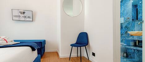 A hotel room with a bed, a chair, a mirror, and a bathroom with a blue marble wall.