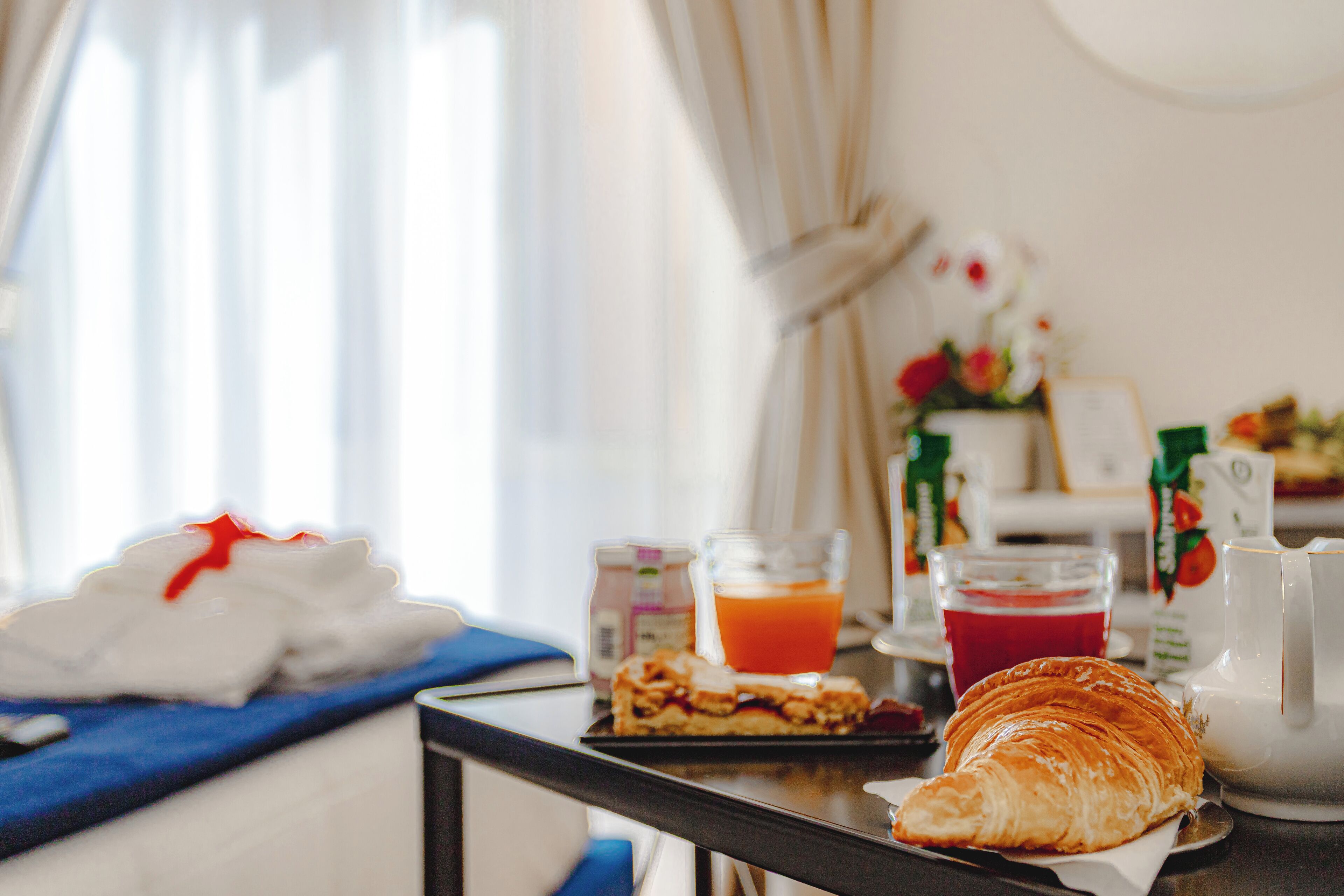 A breakfast table with a croissant, juice, and a coffee pot.