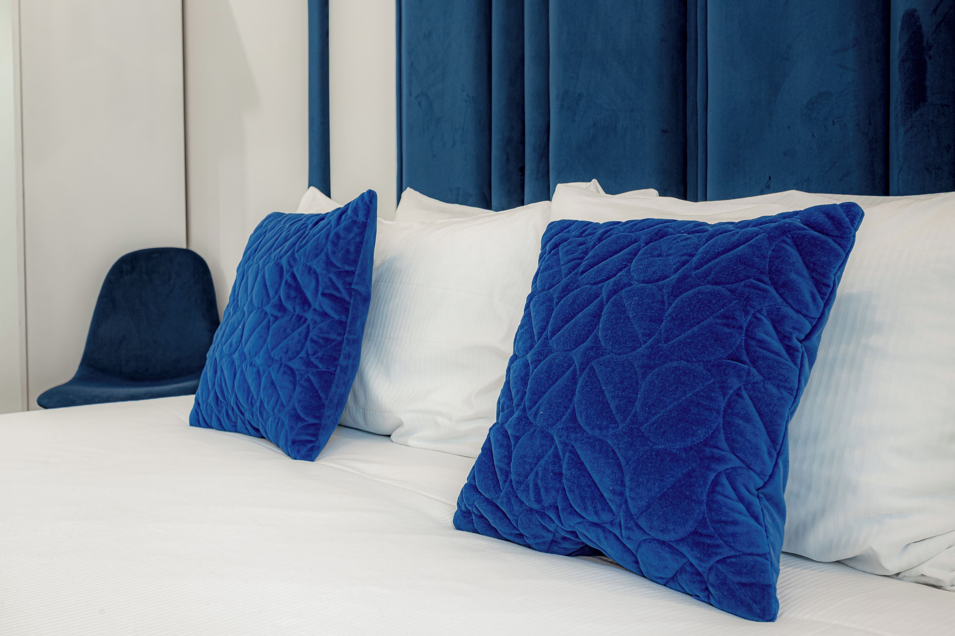 Una cama con sábanas blancas y dos almohadas azules grandes.