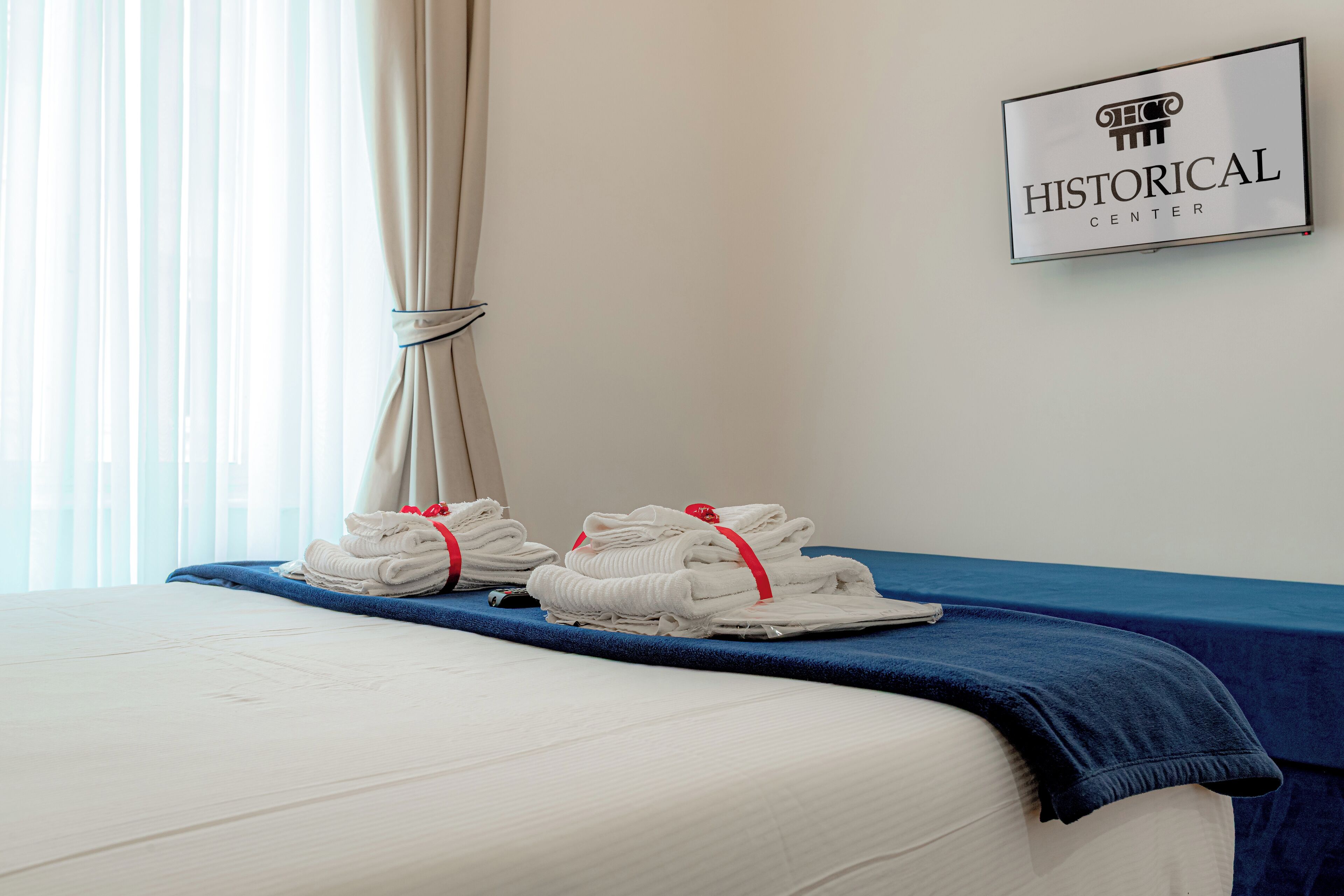 Una cama bien hecha con ropa de cama y toallas blancas, una colcha azul y un cartel en la pared que dice "Historical Center".