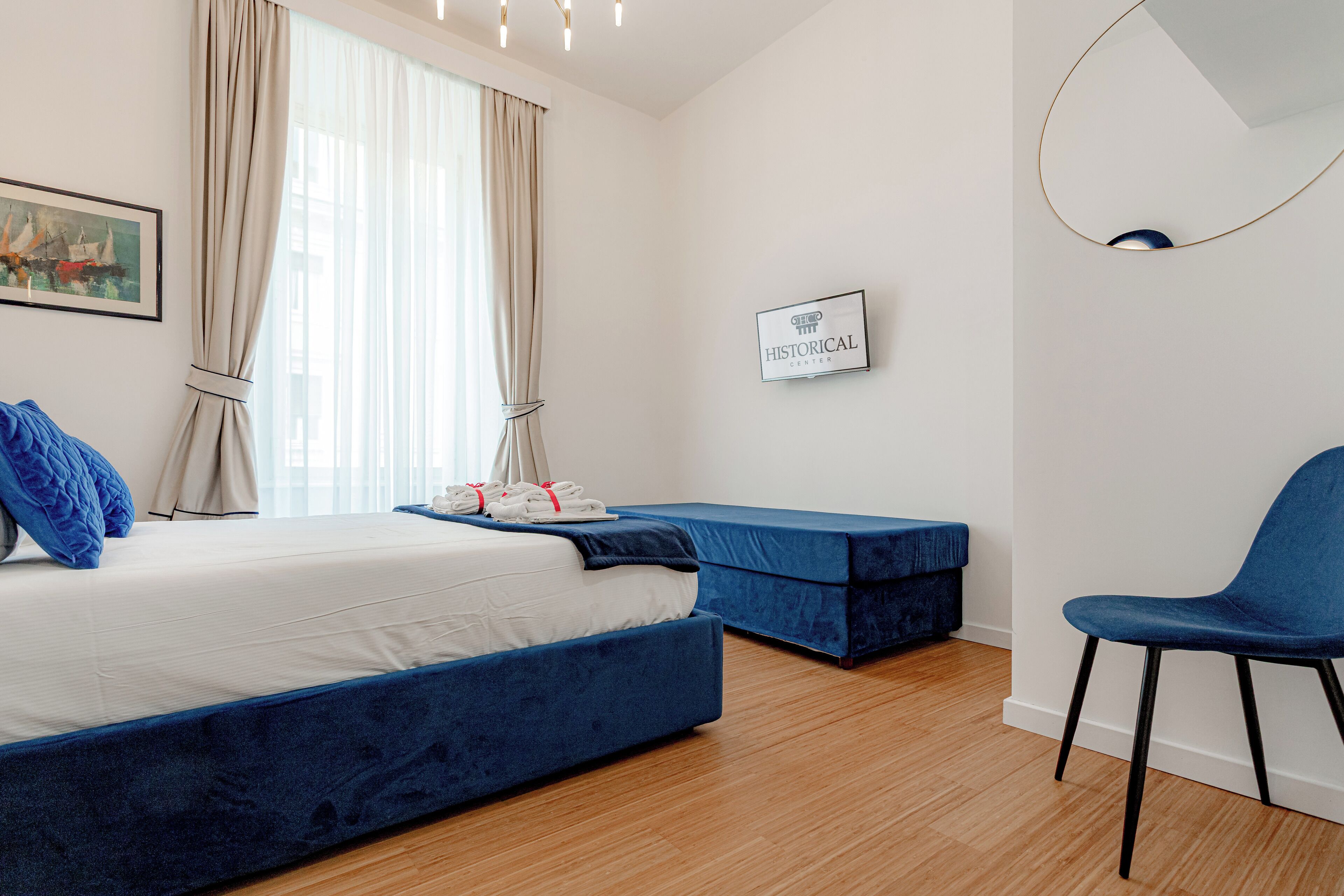 A modern hotel room with a large bed, a blue sofa, a chair, and a painting on the wall.