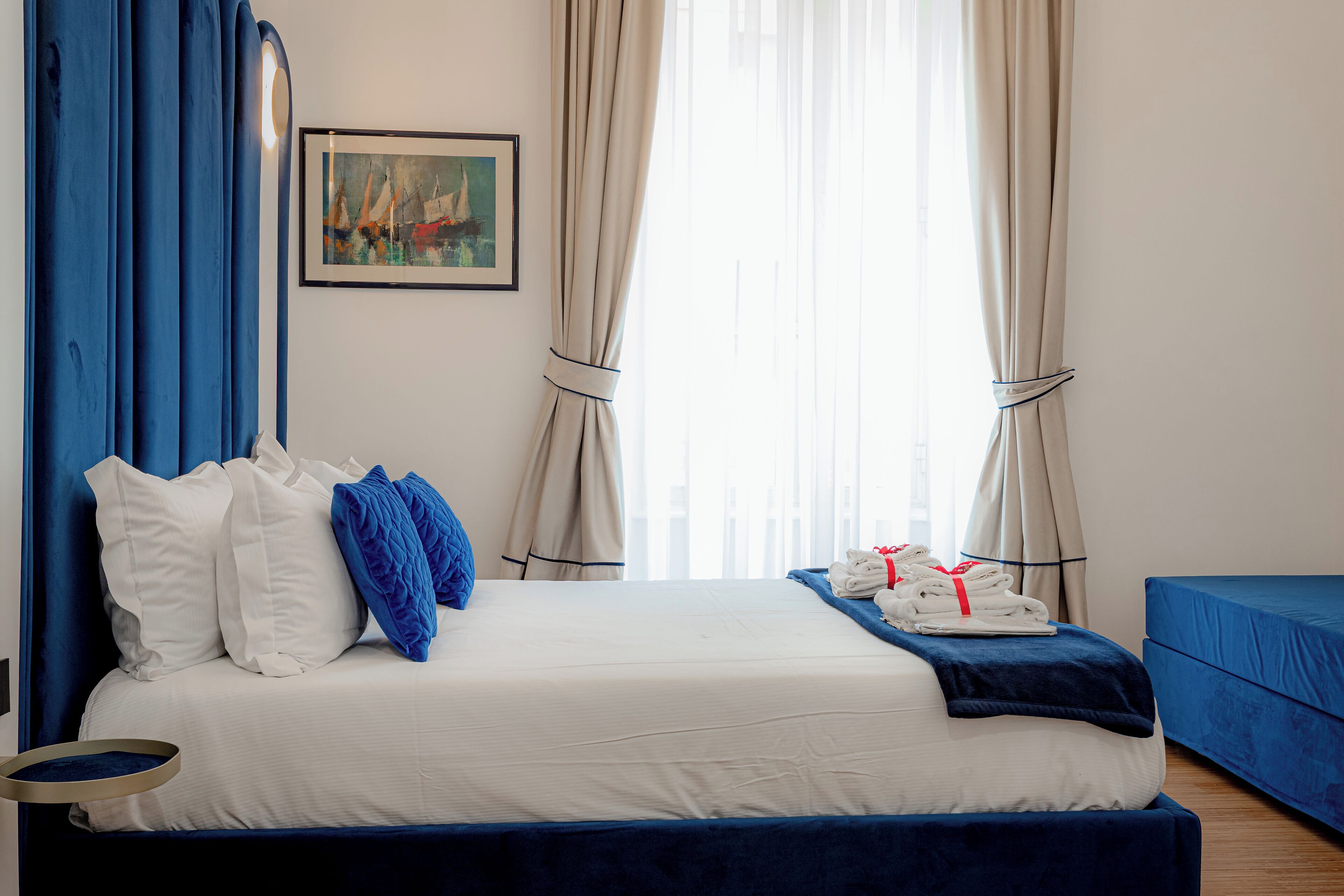 A neatly made bed with white and blue bedding, a blue headboard, and a small bedside table.