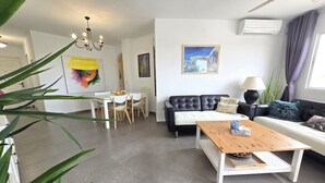 Un salon moderne avec un canapé en cuir noir, une table basse en bois et un coin repas avec des chaises blanches.
