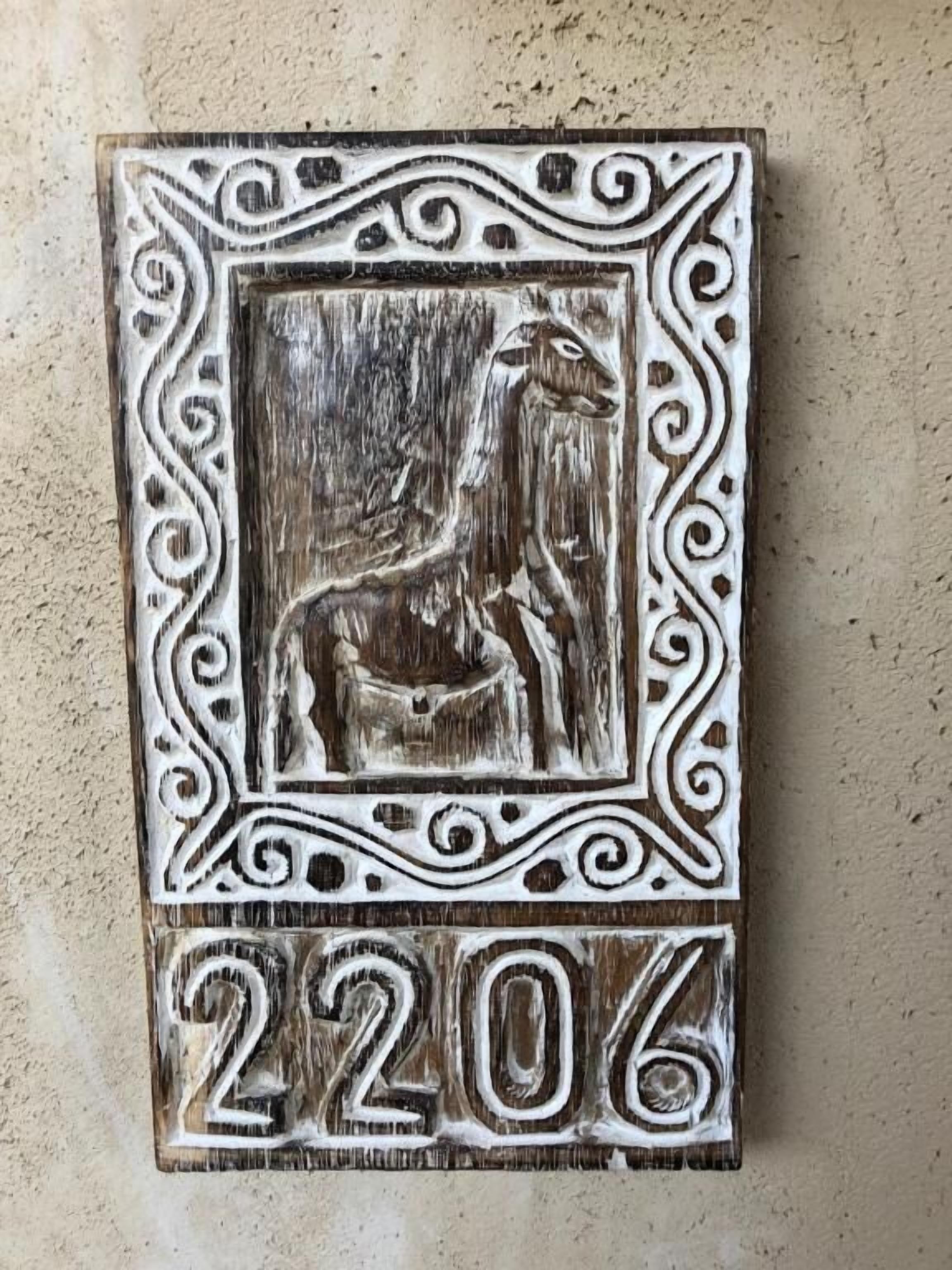 A rustic wooden plaque with a carved horse and rider, surrounded by ornate patterns, and the number 2206.