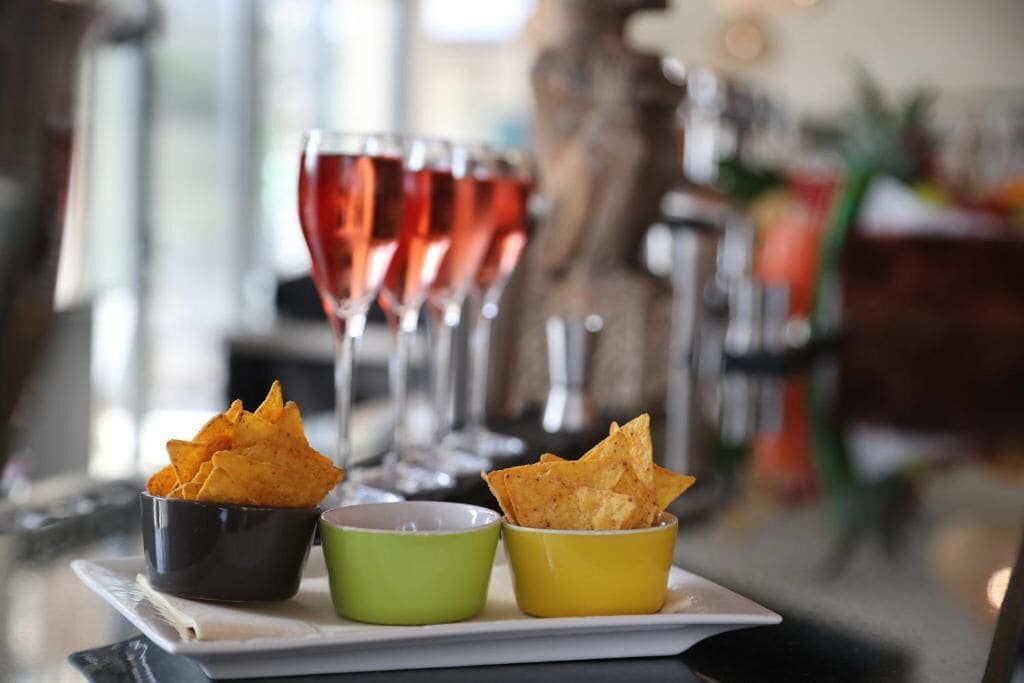 A table with three bowls of chips and two glasses of red drink.