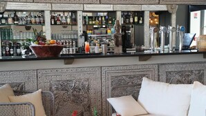 Un espace bar avec un assortiment de bouteilles, un panier de fruits et un coin salon comprenant un canapé et des fauteuils.