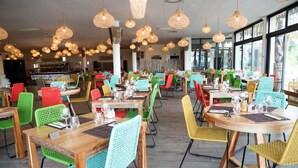 Un comedor amplio con varias mesas y sillas, que destaca por una variedad de colores y lámparas colgantes de estilo mimbre.